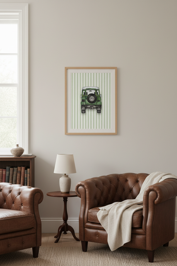 A framed art print featuring a green vintage car on a striped background, displayed on a light beige wall in a styled living room with brown leather armchairs and a side table.