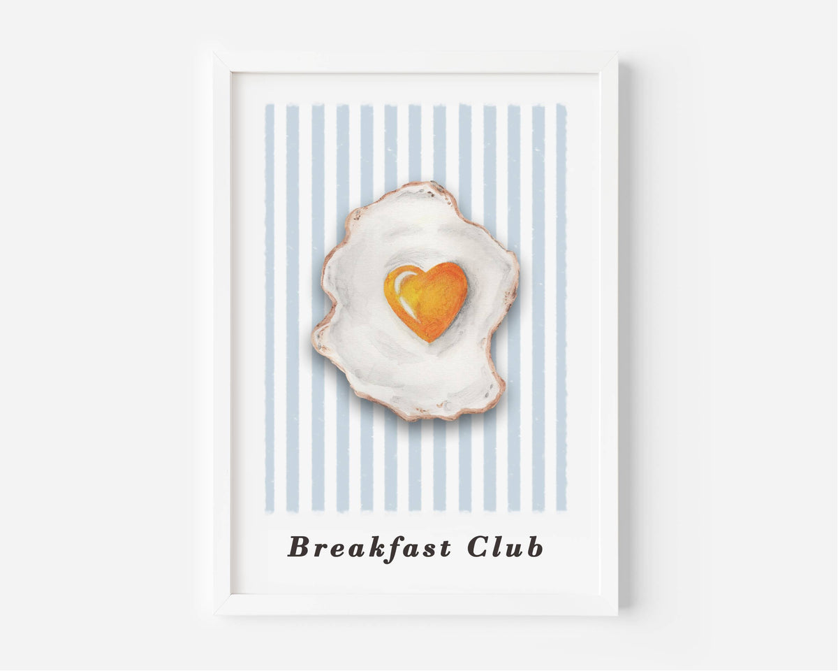 A framed art print featuring a watercolor-style fried egg with a heart-shaped yellow yolk on a background of light blue and white vertical stripes, with the text 'Breakfast Club' printed below.