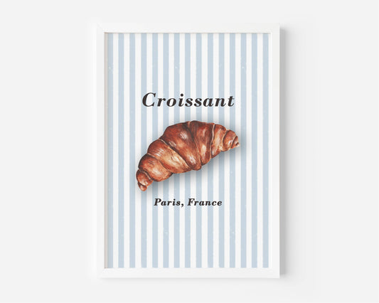 A framed wall art print featuring a croissant illustration on a light blue and white striped background, with the word 'Croissant' and 'Paris, France' printed in black text.