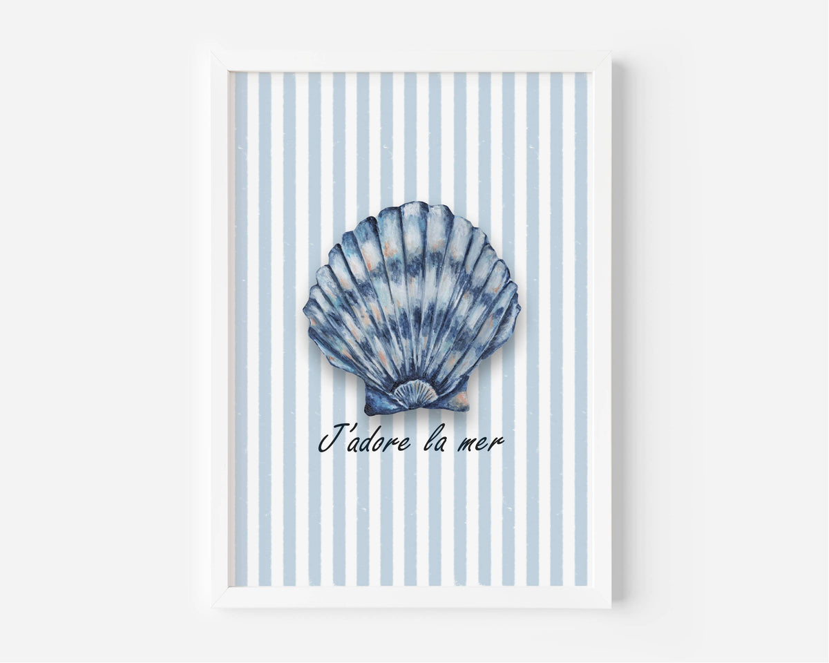 A framed wall art print featuring a blue scallop shell illustration centered on a white and light blue striped background, with the French text 'J'adore la mer' below. The print is shown in a white frame against a light gray wall.