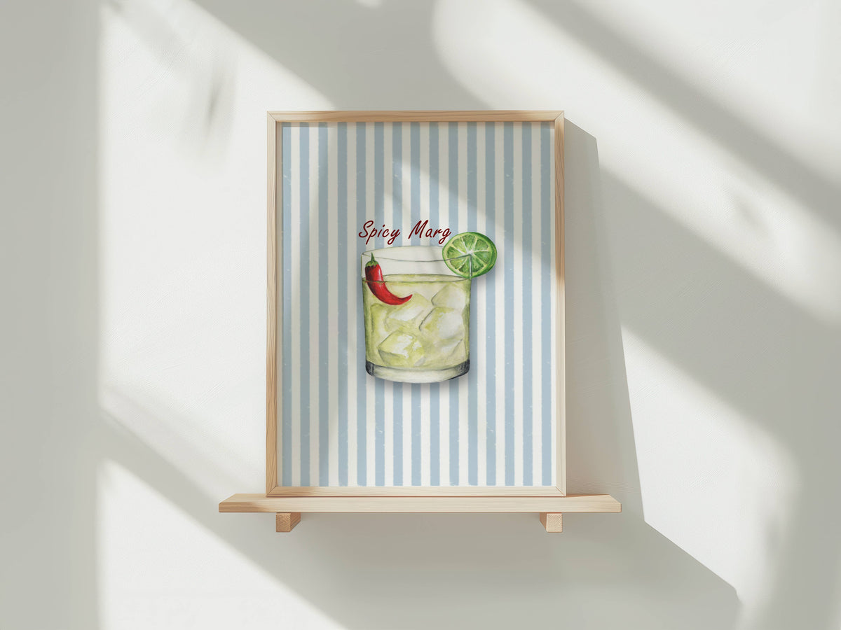 A framed art print featuring a colorful illustration of a spicy margarita on a light blue and white striped background, displayed on a wooden easel against a white wall with soft window shadows.