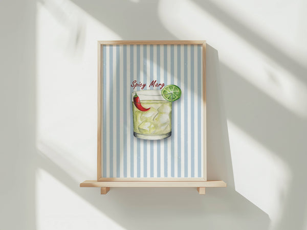 A framed art print featuring a colorful illustration of a spicy margarita on a light blue and white striped background, displayed on a wooden easel against a white wall with soft window shadows.