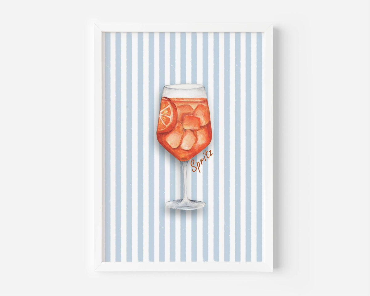 A framed art print featuring a watercolor illustration of a glass of orange soda with ice and a lemon slice, set against a background of vertical light blue and white stripes. The word 'Spirits' is written in a cursive font near the glass.