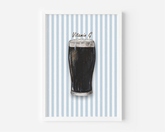 A framed art print featuring a dark pint of stout on a background of vertical light blue and white stripes, with the text 'Vitamin B' written above the drink. The print is housed in a clean white frame and is displayed against a neutral light gray wall.