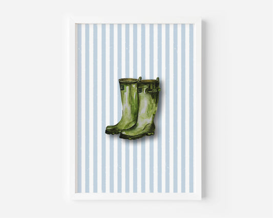 A framed art print featuring a pair of green rain boots centered on a background of light blue and white vertical stripes, displayed against a clean white wall.