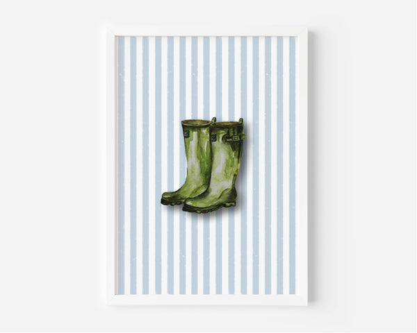 A framed art print featuring a pair of green rain boots centered on a background of light blue and white vertical stripes, displayed against a clean white wall.