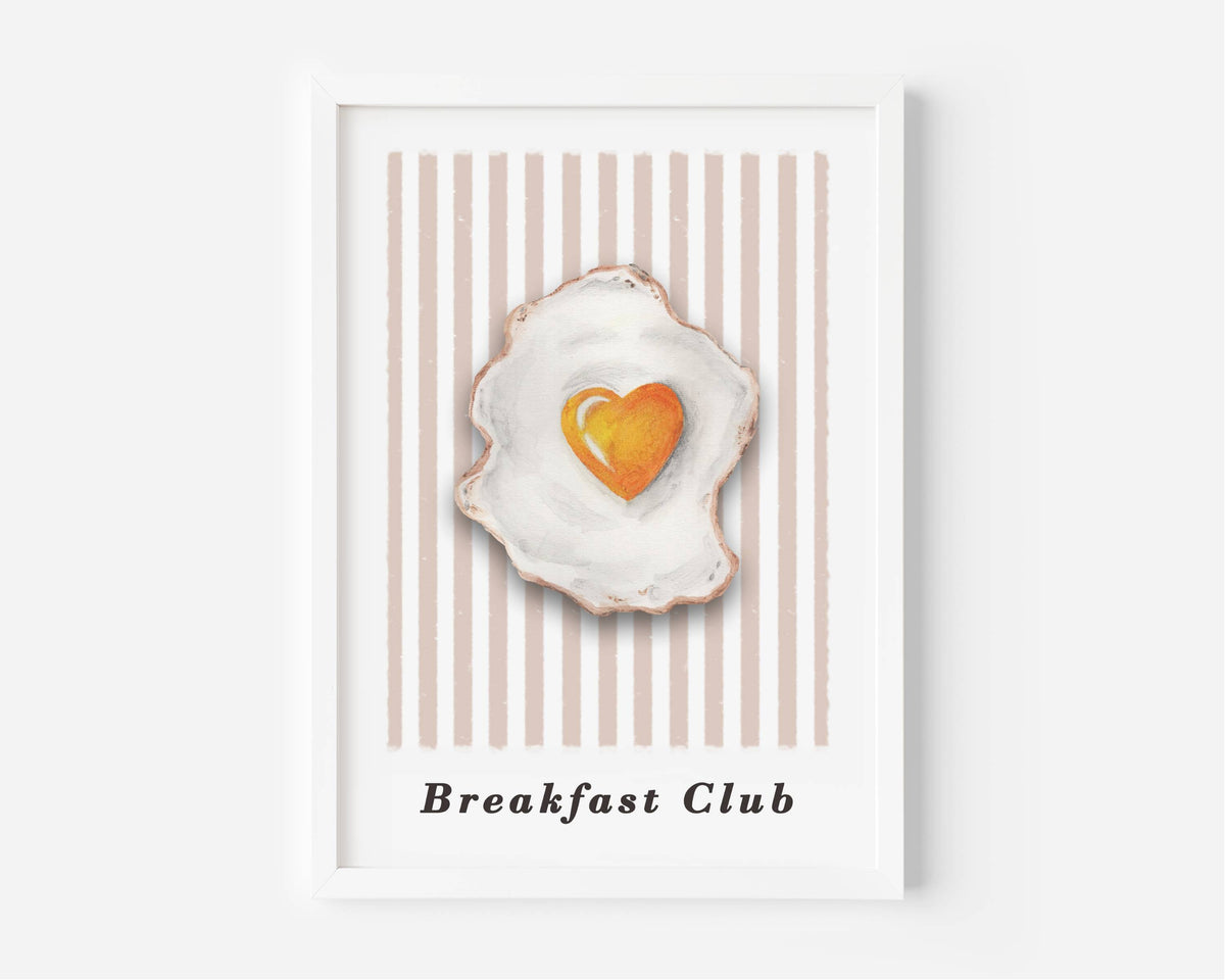 A framed art print featuring a watercolor-style fried egg with a heart-shaped yellow yolk, set against a background of vertical beige and white stripes. The text 'Breakfast Club' is printed at the bottom.