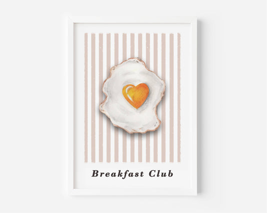 A framed art print featuring a watercolor-style fried egg with a heart-shaped yellow yolk, set against a background of vertical beige and white stripes. The text 'Breakfast Club' is printed at the bottom.