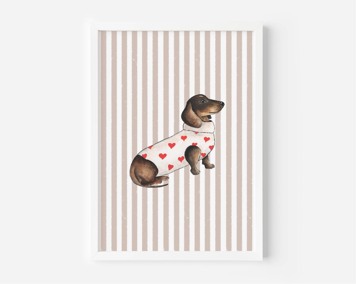 A framed art print featuring a watercolor illustration of a dachshund wearing a white sweater with red hearts, set against a background of vertical beige and white stripes.