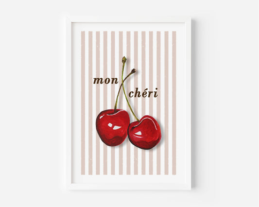 A framed art print featuring two red cherries with the French text 'mon chéri' on a background of vertical beige and pink stripes, set against a clean white wall.