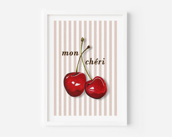A framed art print featuring two red cherries with the French text 'mon chéri' on a background of vertical beige and pink stripes, set against a clean white wall.