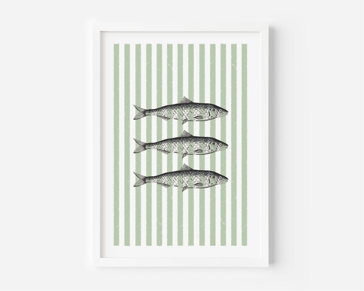 Framed wall art featuring three horizontal fish illustrations centered on a background of vertical sage green and white stripes, shown in a white frame against a light gray wall.