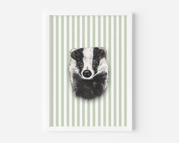 A framed art print featuring a black and white sketch of a badger's face centered on a background of vertical sage green and white stripes, displayed on a clean white wall.