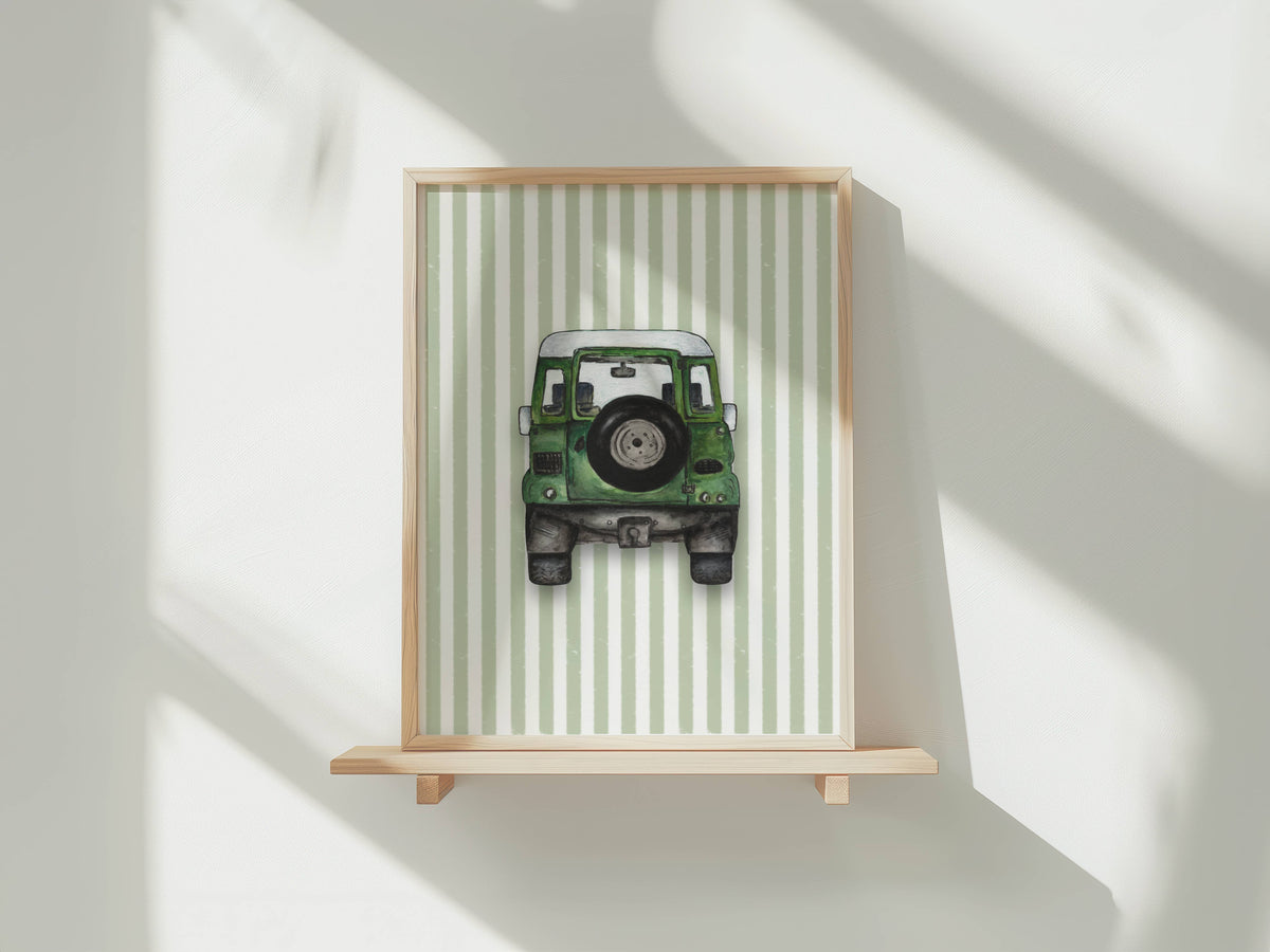 A framed art print featuring a green vintage jeep on a light green and white striped background, displayed on a light wood shelf against a white wall with soft window shadows.