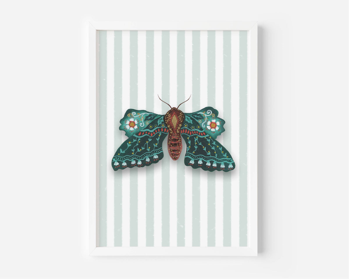 A framed art print featuring a detailed teal and brown moth with orange accents on a background of pale mint green and white vertical stripes, set against a clean white wall.