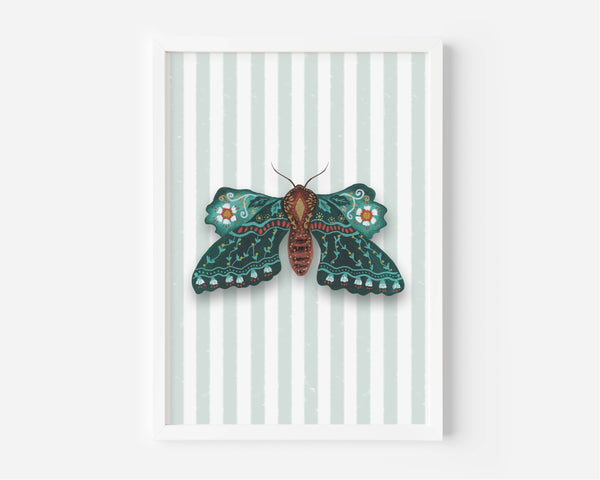 A framed art print featuring a detailed teal and brown moth with orange accents on a background of pale mint green and white vertical stripes, set against a clean white wall.