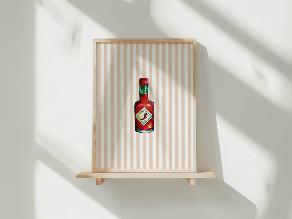 A framed art print featuring a stylized painting of a Tabasco bottle on a beige and white striped background, displayed on a light wood floating shelf against a white wall with soft window shadows.