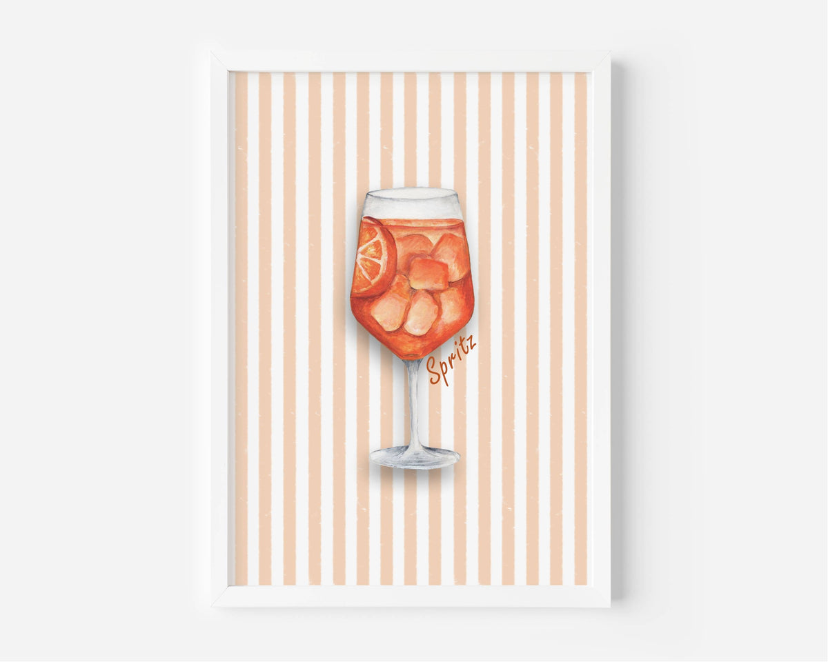 A framed art print featuring a watercolor illustration of a glass of orange soda with ice and a lemon slice, set against a background of vertical peach and white stripes. The print is housed in a simple white frame and is displayed against a neutral light gray wall.