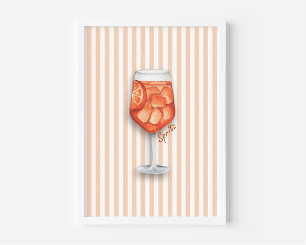 A framed art print featuring a watercolor illustration of a glass of orange soda with ice and a lemon slice, set against a background of vertical peach and white stripes. The print is housed in a simple white frame and is displayed against a neutral light gray wall.