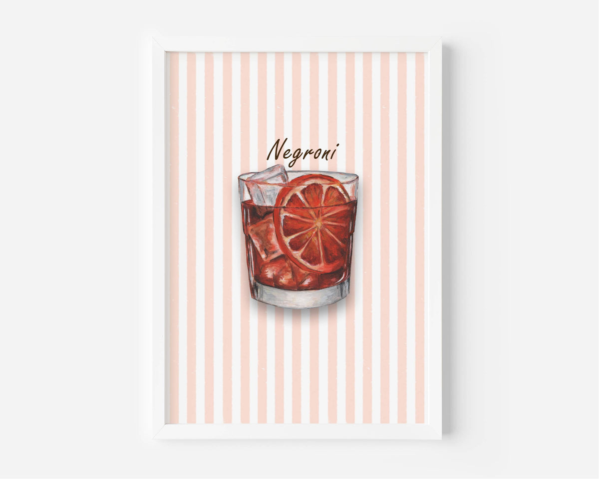 A framed art print featuring a watercolour illustration of a Negroni cocktail in a tumbler glass with ice and an orange slice garnish, set against a background of vertical coral and white stripes. The print is shown in a white frame against a light grey wall.