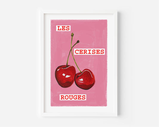 A framed art print featuring two red cherries on a pink background with the French text 'LES CERISES ROUGES' in white lettering, displayed on a light gray wall.