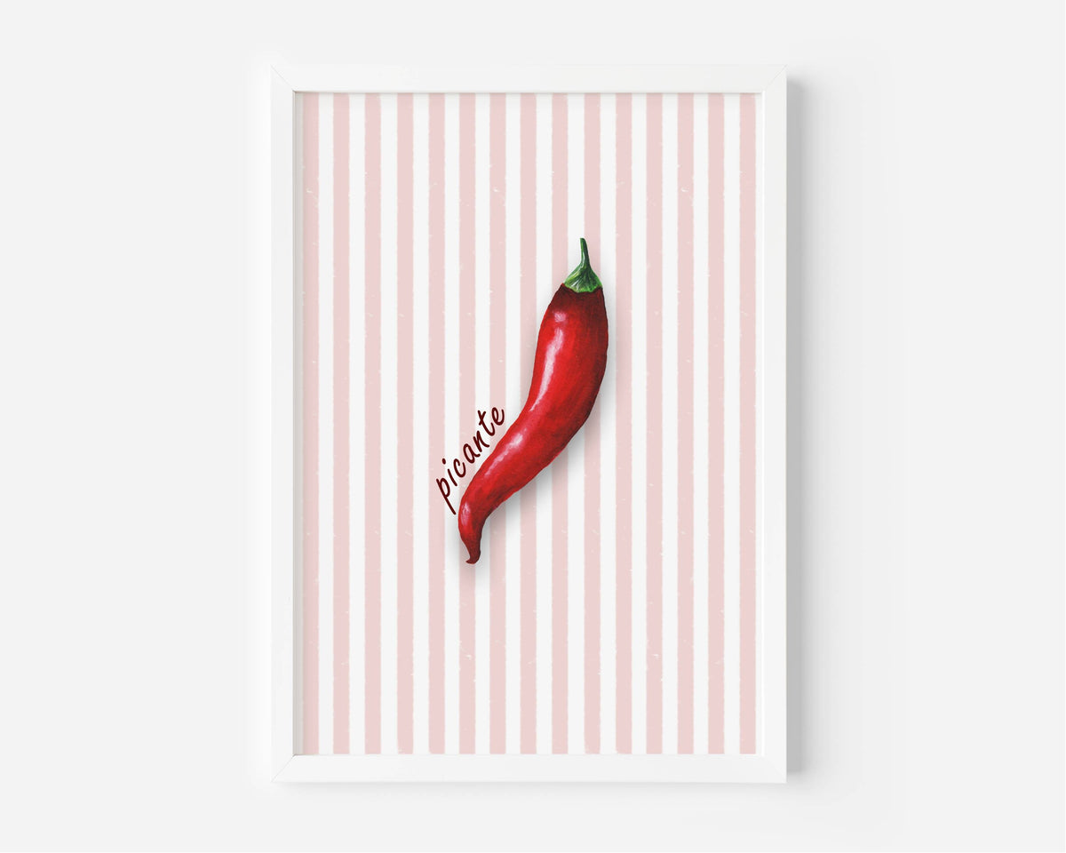 A framed wall art print featuring a single red chili pepper on a white and pale pink striped background, with the word 'picante' written in script. The print is shown in a white frame against a light gray wall.