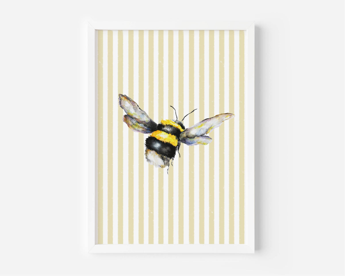 A framed art print featuring a watercolor bumblebee centered on a background of vertical cream and pale yellow stripes, set against a clean white wall.