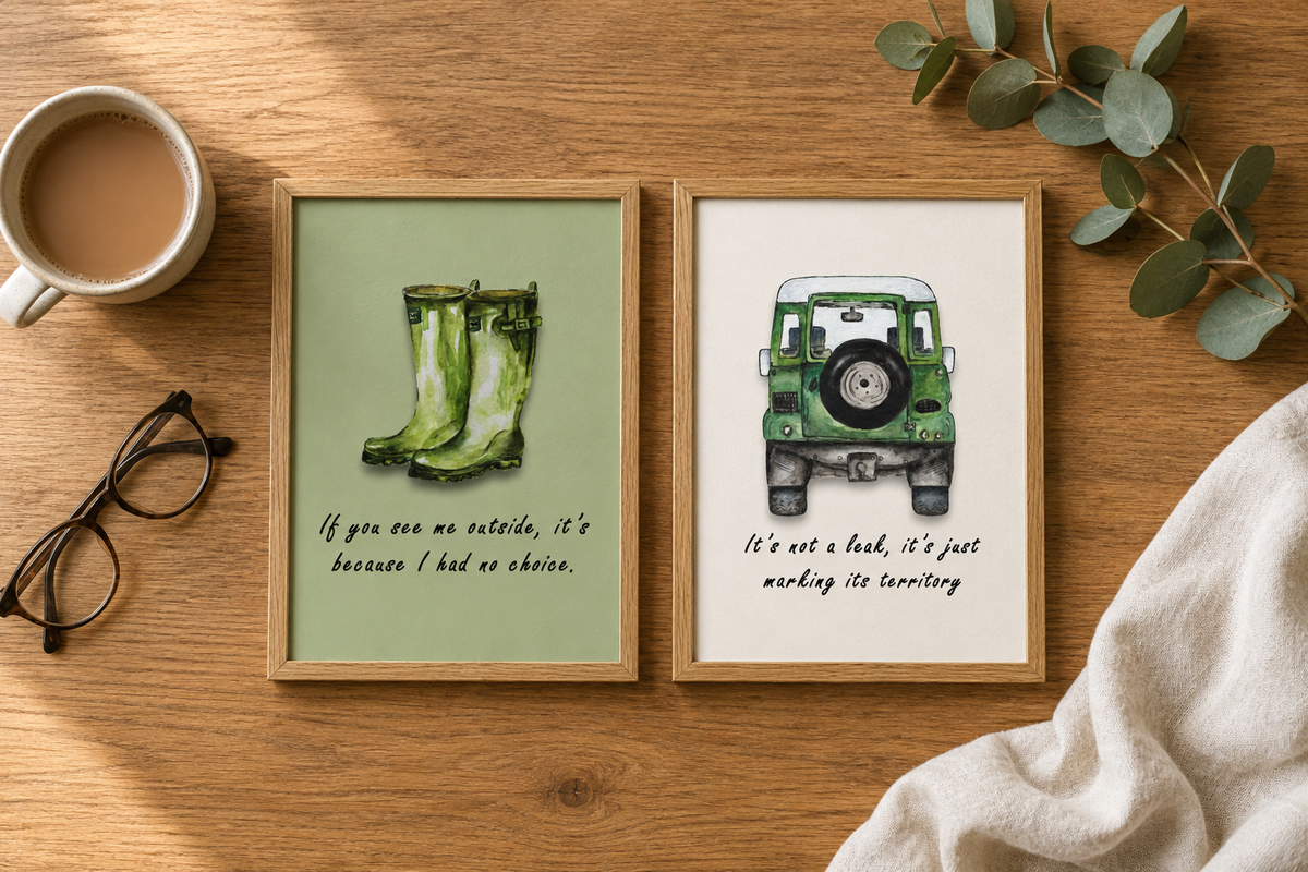 Flat-lay of two A5 watercolour art prints in oak frames on a wooden table with a mug, reading glasses and eucalyptus, showing green wellington boots and a green classic 4x4 with hand-lettered text.