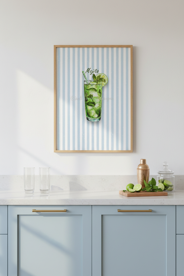 A framed art print featuring a mojito cocktail with light blue and white vertical stripes, hanging on a white wall above a light blue kitchen cabinet with gold handles.