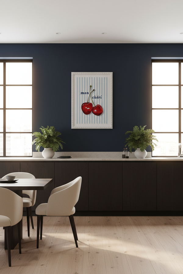 A framed wall art print featuring two red cherries on a white and light blue striped background with the text 'mon cheri', displayed in a modern dining room setting against a dark navy blue wall.