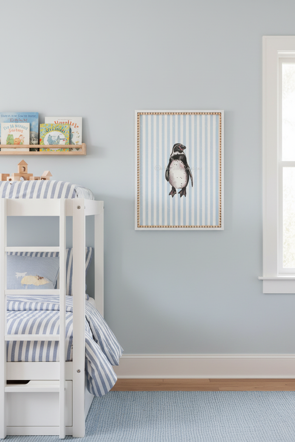 A framed vertical art print of a penguin on blue and white striped paper, hanging on a light blue-gray wall in a styled children's bedroom with a white bunk bed and blue striped bedding.