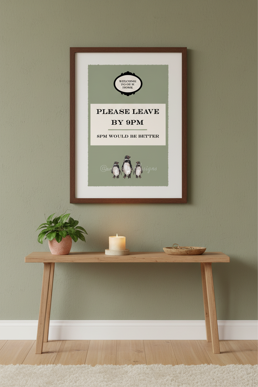 A framed art print featuring a vintage-style 'Please Leave By 9pm' sign with penguin illustrations, displayed on a sage green wall above a wooden console table with a plant and candle.