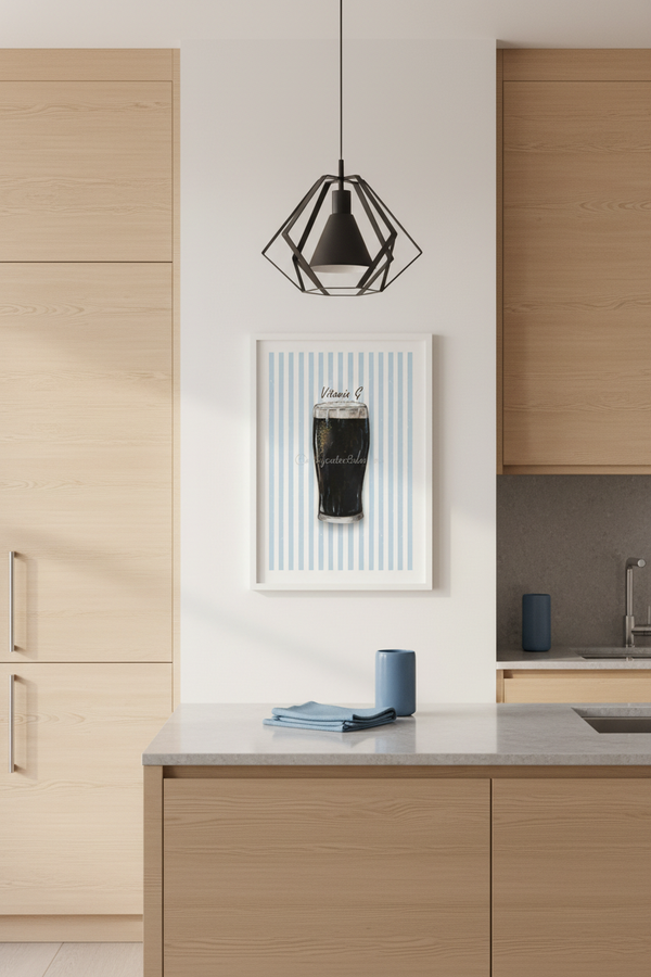 A modern kitchen interior with light wood cabinetry, a gray countertop, a black geometric pendant light, and a framed vertical art print on the wall depicting a dark beer glass against light blue stripes.